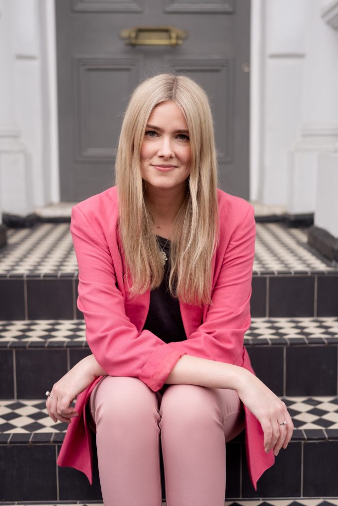 blonde lady smiling on checkered steps in Notting Hill wearing pink suit