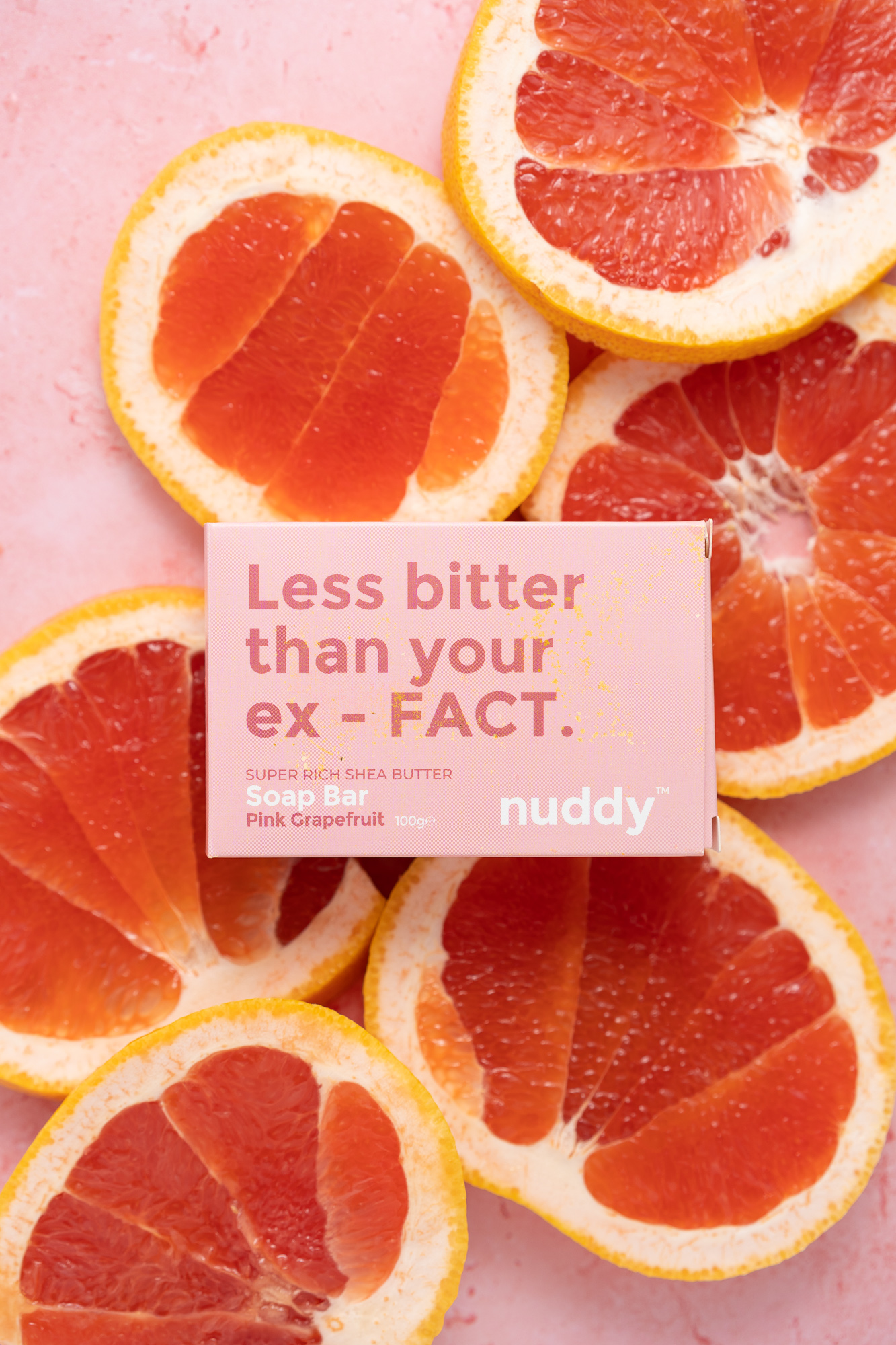 studio product photography of nuddy soap bar in pink grapefruit surrounded by slices of pink grapefruit on pink backdrop